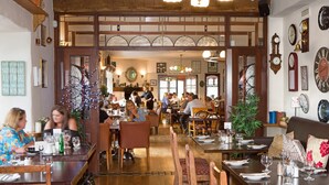 Een restaurant met houten meubels, meerdere eettafels en diverse klokken aan de wanden.