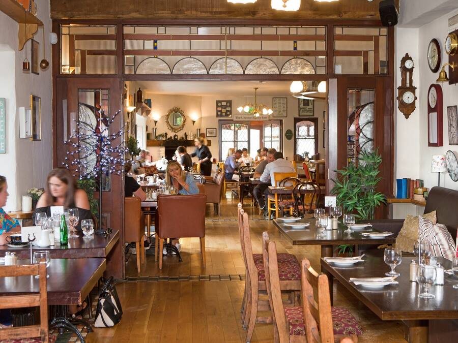 A restaurant with wooden furniture, multiple dining tables, and a variety of clocks on the walls.