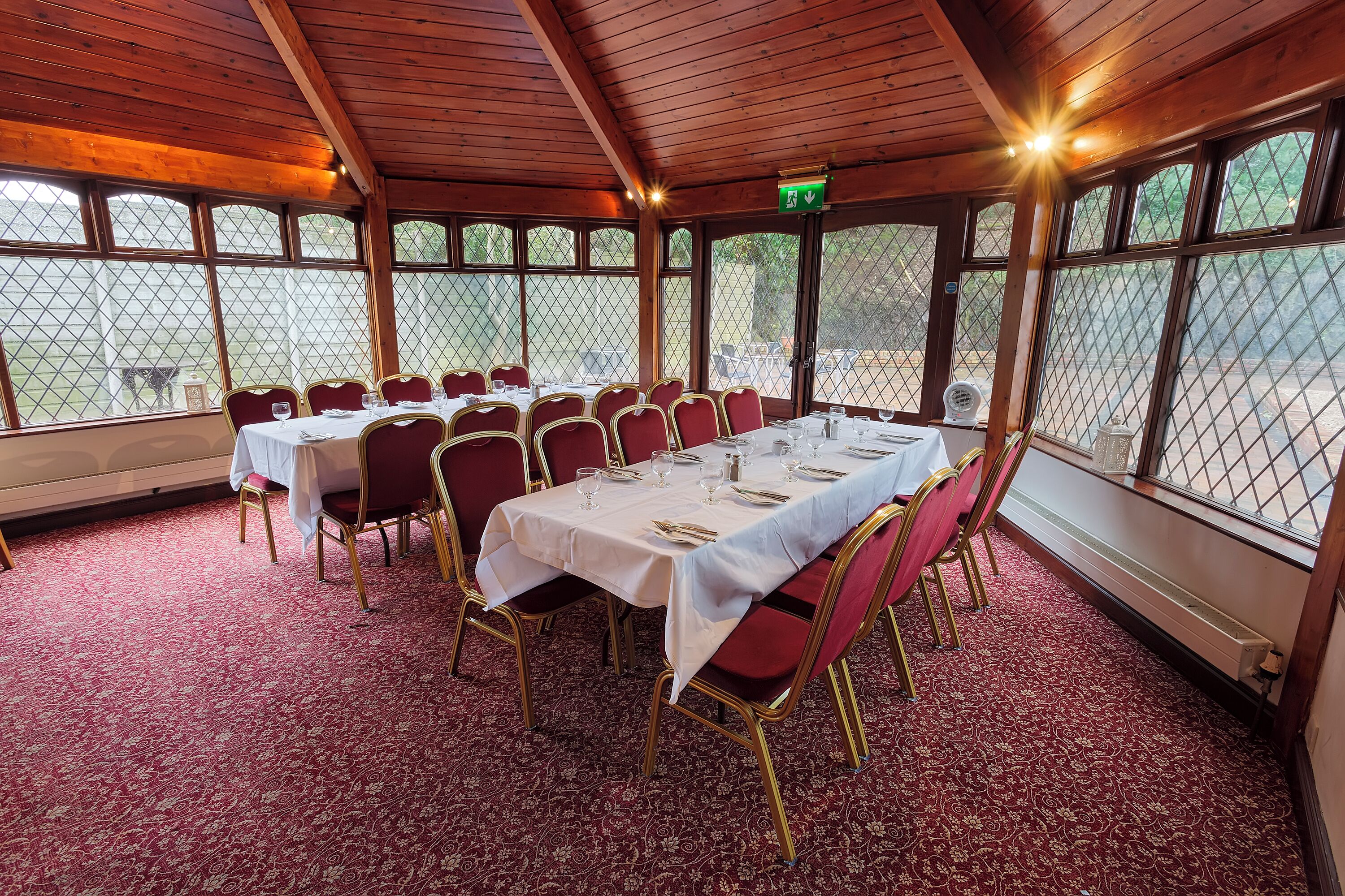 A dining area with tables set for six, red chairs, and a red carpeted floor.