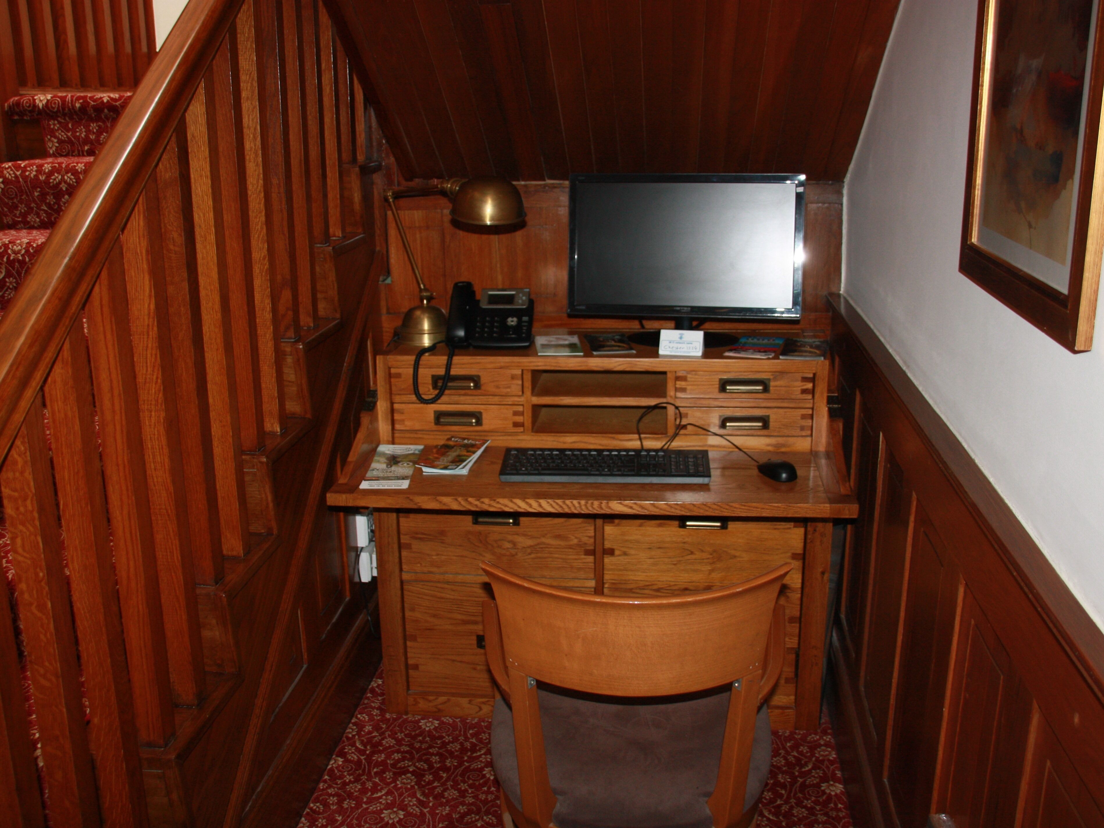 A wooden desk with a computer, keyboard, and lamp in a corner.