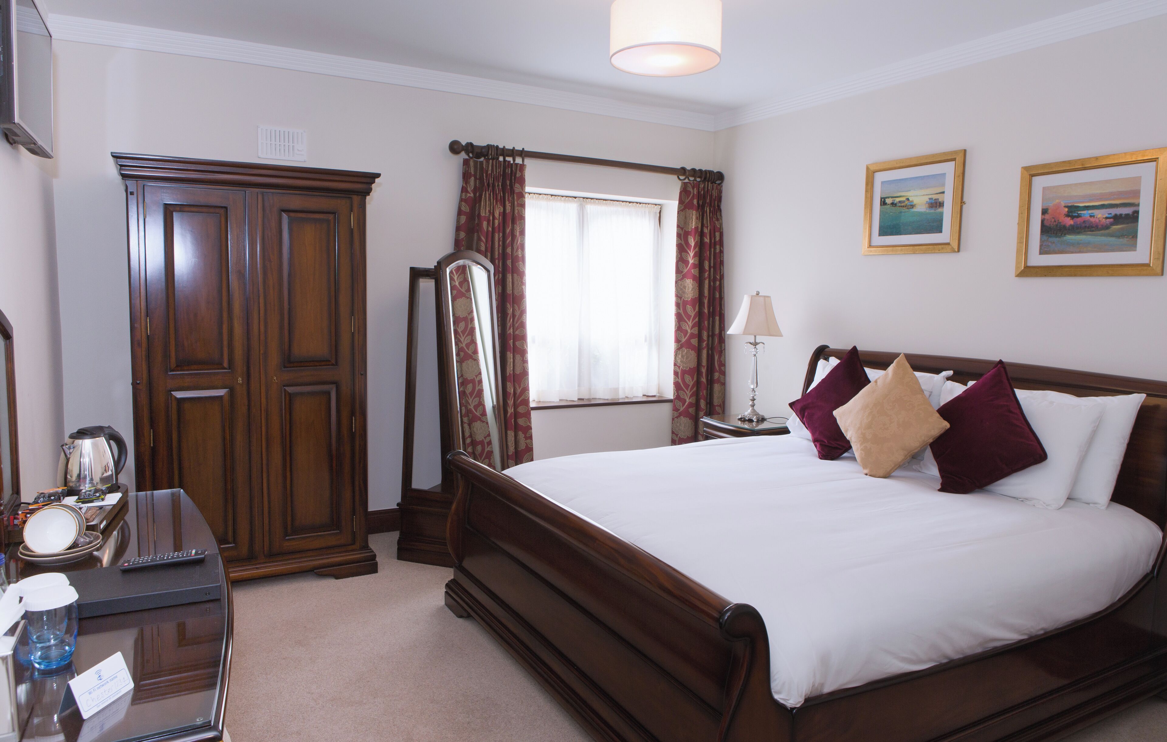 A bedroom with a large wooden bed, a dresser, a mirror, and two framed pictures on the wall.