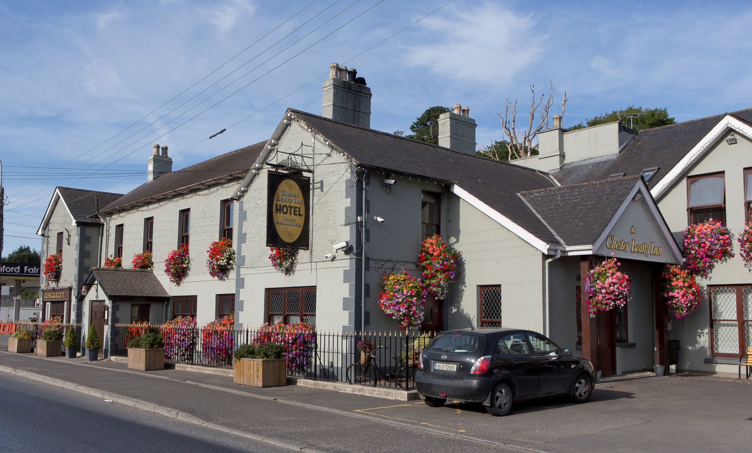 Un edificio tradicional con un letrero que dice Chester Beatty Inn, con macetas de flores y un coche estacionado frente a él.