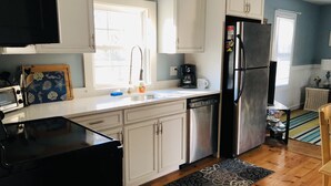 A modern kitchen with white cabinets, a stainless steel refrigerator, a dishwasher, and a window providing natural light. - Renovated Cottage with nice yard and homey interior (Edgartown)