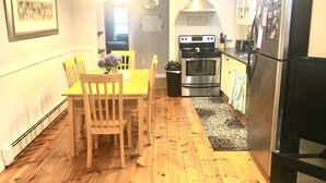 A kitchen with wooden flooring, a dining table with chairs, a stove, an oven, and a refrigerator. - Renovated Cottage with nice yard and homey interior (Edgartown)
