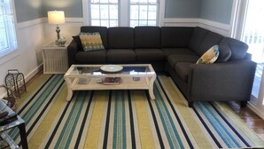 A living room with a dark brown sectional sofa, a glass coffee table, a striped rug, and a lamp on a side table. - Renovated Cottage with nice yard and homey interior (Edgartown)