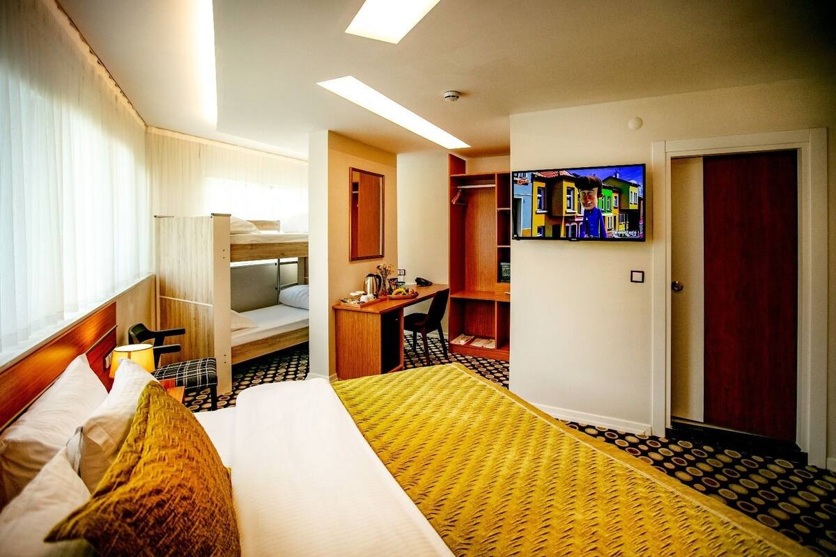 A hotel room with a bunk bed, a desk, a chair, a television, and a bookshelf.
