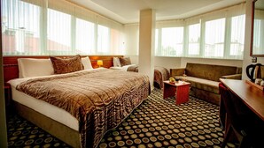 Habitación de hotel con una cama grande, un sofá, una mesita con una bebida y una máquina de café.