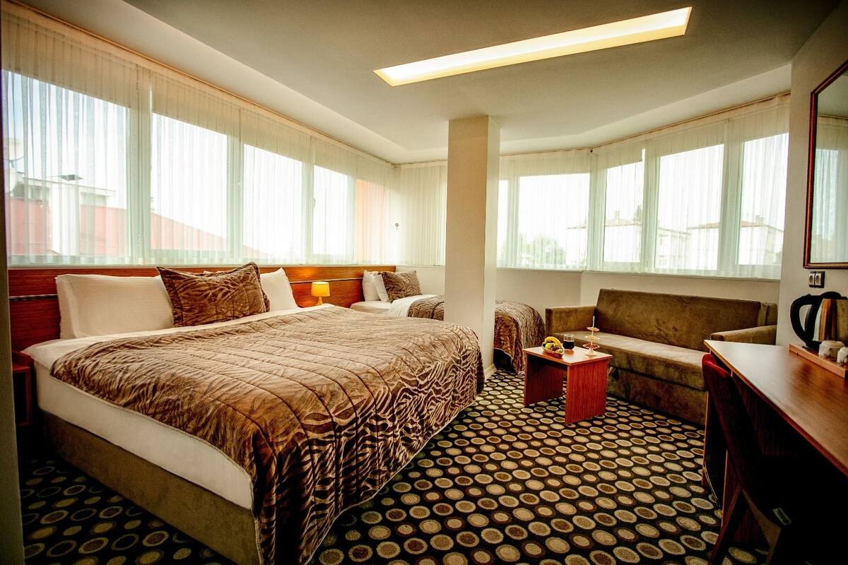 A hotel room with a large bed, a sofa, a small table with a drink, and a coffee machine.