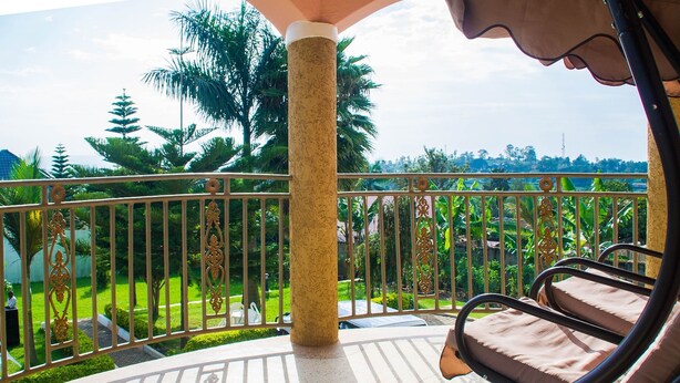 Un balcon doté d’une balustrade en métal, d’un pilier de couleur beige et offrant une vue sur un paysage verdoyant, avec des arbres et une tour située au loin.