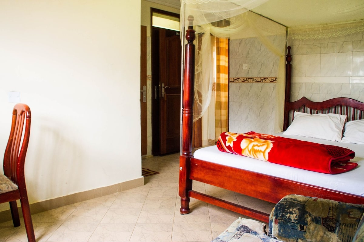 Une chambre à coucher avec un lit à baldaquin, une chaise en bois et une porte donnant sur une autre pièce.