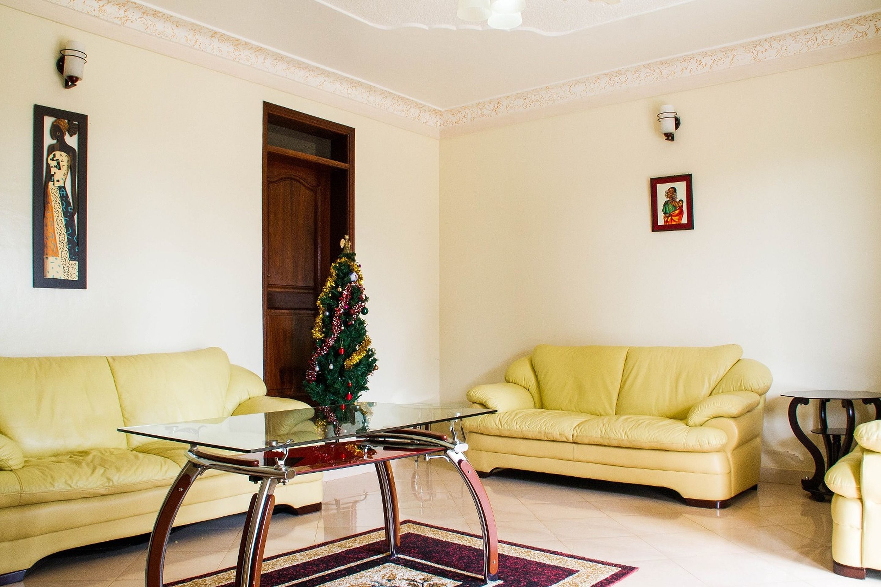A living room with a glass coffee table, two yellow sofas, a Christmas tree, and framed artwork on the walls.