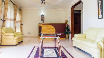 A living room with a wooden sofa, a yellow armchair, a wooden coffee table, and a red-framed mirror.