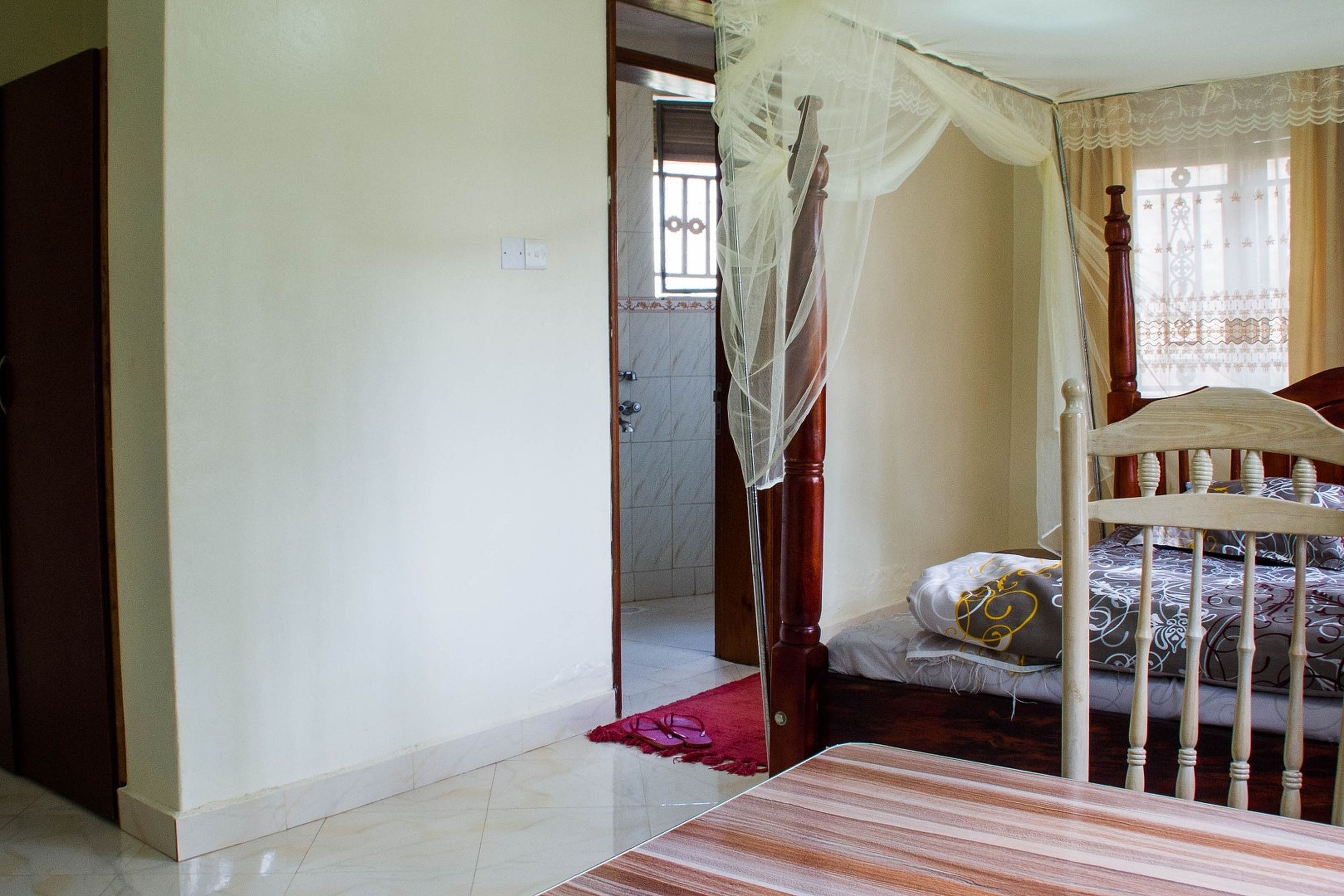 Un dormitorio con una cama, cabecera de madera, mosquitero y alfombra roja.