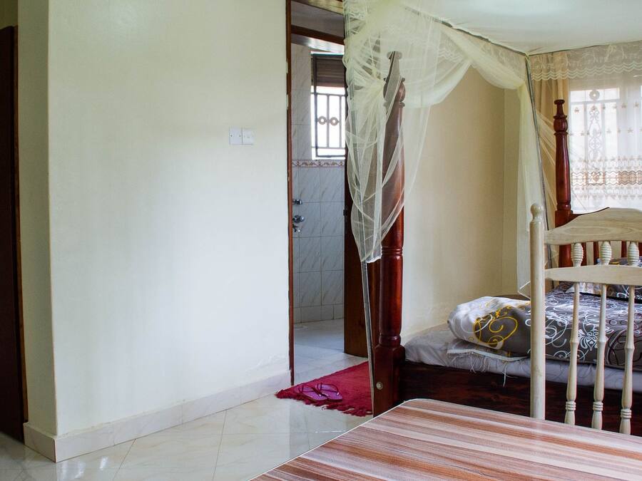 Un dormitorio con una cama, cabecera de madera, mosquitero y alfombra roja.