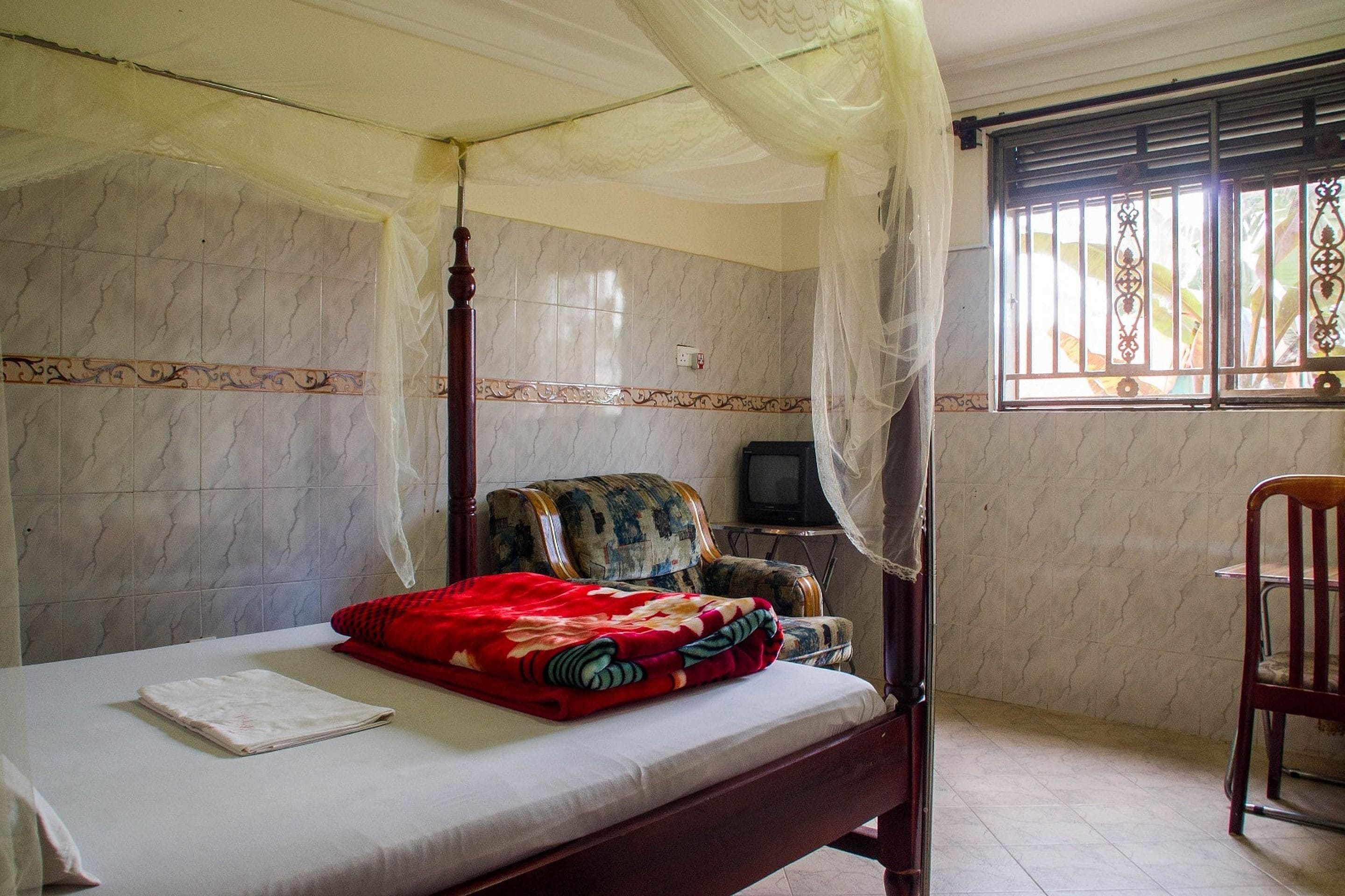 A bedroom with a four-poster bed, a television, and a chair.