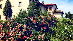 A two-story building with a red-tiled roof, surrounded by lush greenery and flowering plants. - Agriturismo Cantagrillo (Vinci)