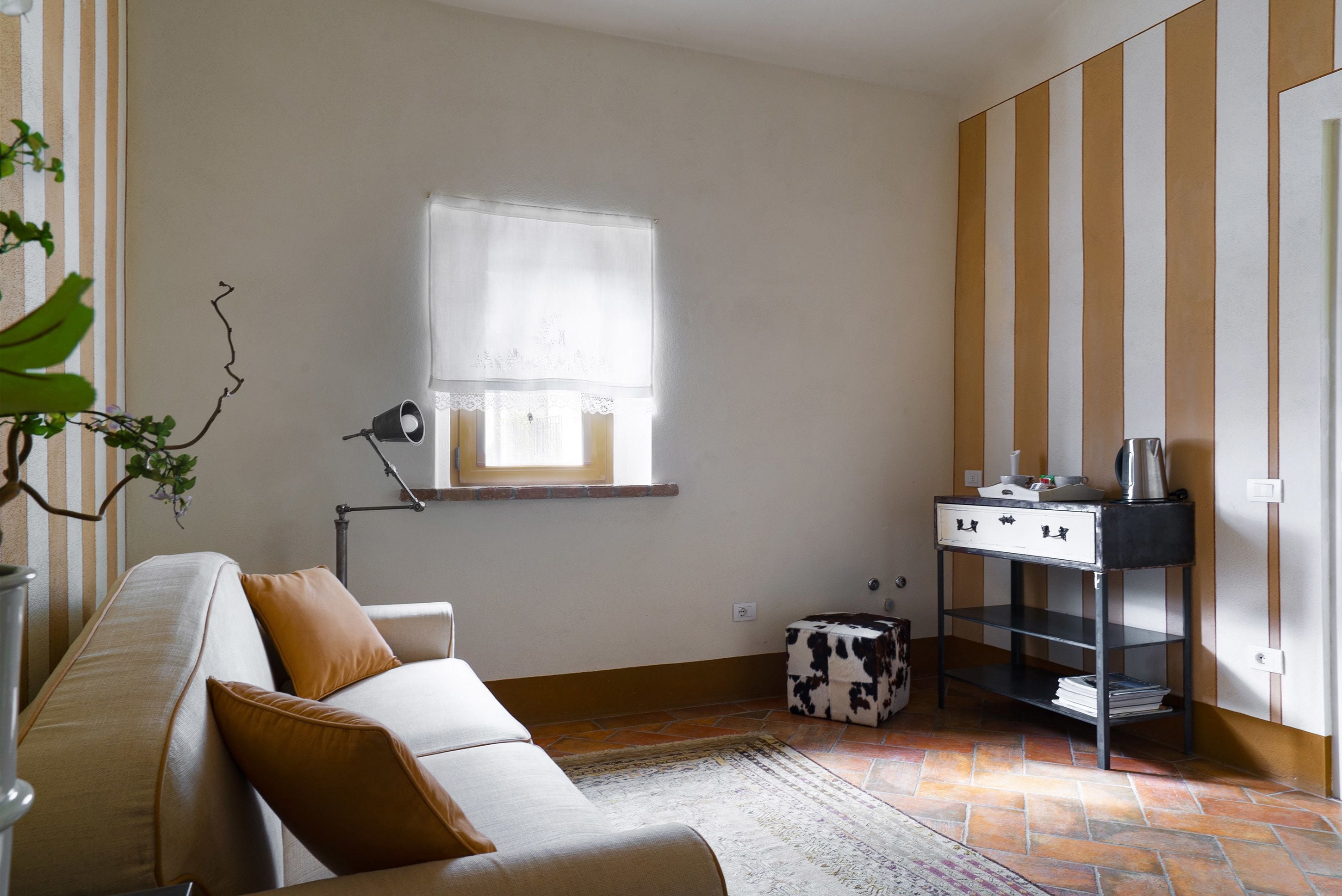 Ein kompakter Wohnraum mit einer Couch, einem kleinen Tisch mit Wasserkocher, einer Heizung und einem Fenster mit Vorhang.