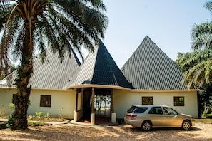 A building with a unique pyramid-shaped roof, a car parked in front, and a palm tree nearby. - Elephant HAB Lodge (Kichwamba)