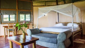 A room with a bed, a wooden table, a chair, and a window with curtains.