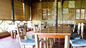 A rustic wooden dining area with a long table and chairs, surrounded by wooden walls and windows.