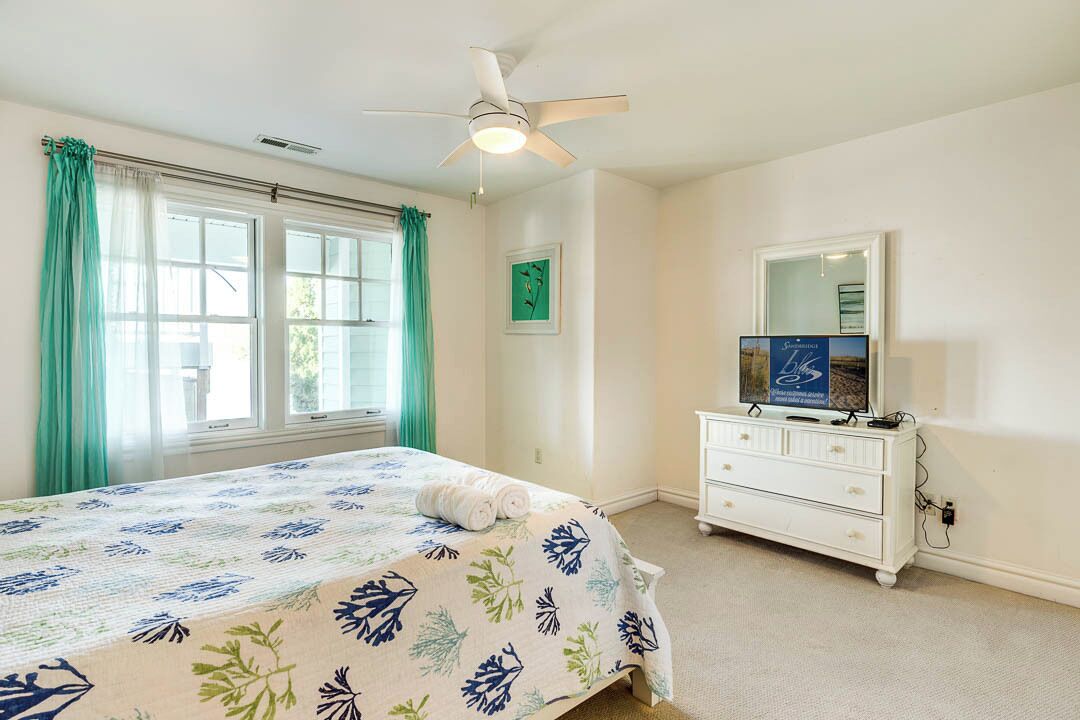 Une chambre à coucher avec un lit, un ventilateur de plafond, une commode et un téléviseur.