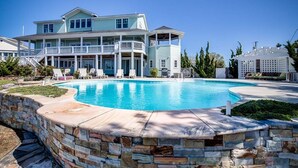 Una casa grande con piscina, un porche cubierto y un muro de contención de piedra.