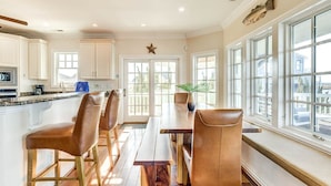 Una cocina moderna con armarios blancos, una isla central con taburetes y ventanas amplias con vistas al exterior.