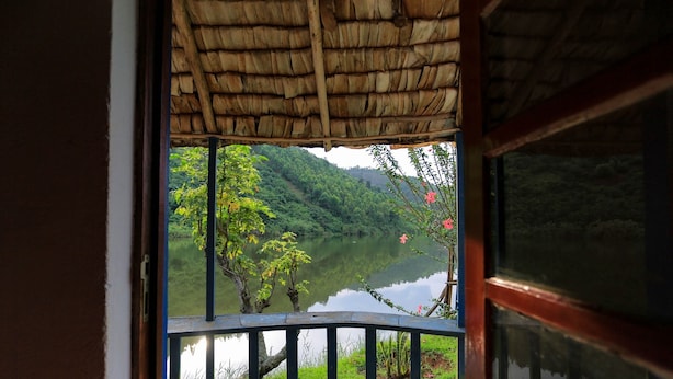 A view from a balcony with a thatched roof, overlooking a calm lake and lush greenery. - Hakurya Gasabo Lodge (Kigali)