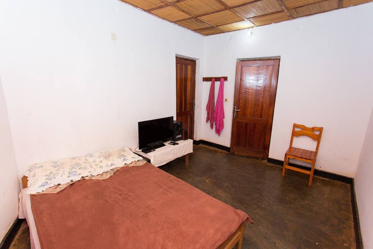 A small, simple room with a bed, a television on a table, and two wooden doors.