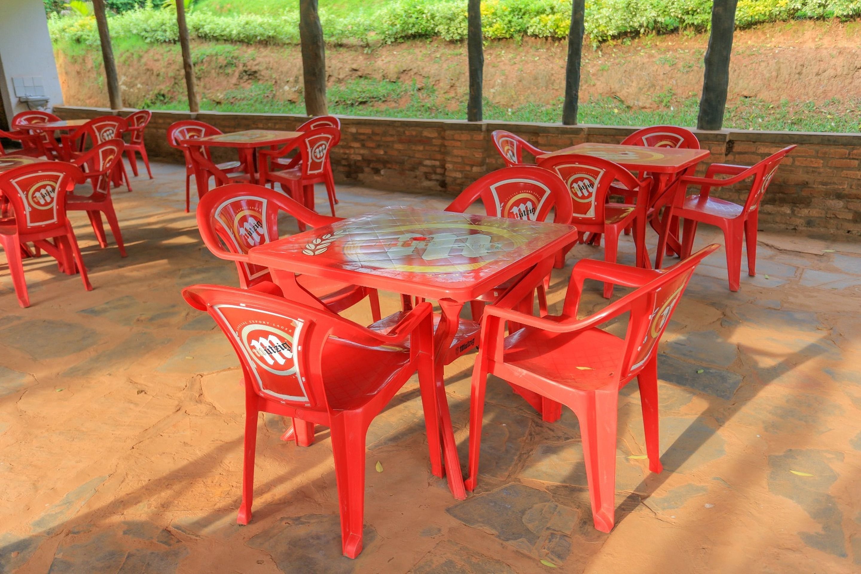 A covered outdoor seating area with red plastic chairs and tables, arranged in a circular pattern.