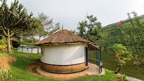 A circular building with a thatched roof, surrounded by greenery and a body of water. - Hakurya Gasabo Lodge (Kigali)