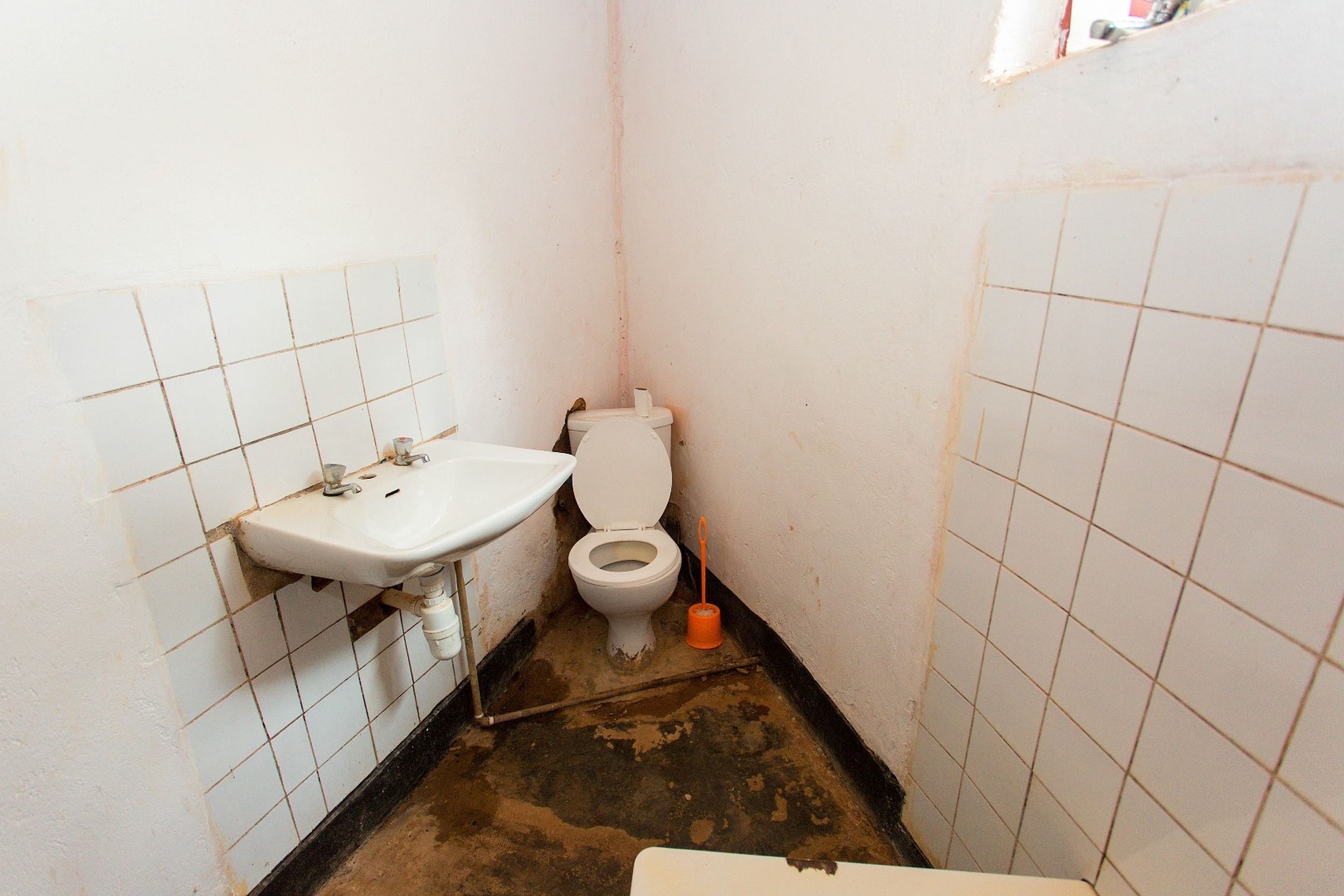A small, narrow bathroom with a white sink, toilet, and visible dirt on the floor.