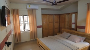 Un dormitorio con cama, armario de madera, ventilador de techo y televisor montado en la pared.