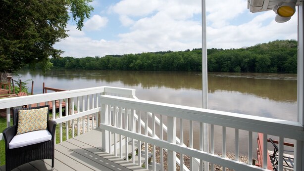 A deck with a white railing overlooking a river, surrounded by greenery.