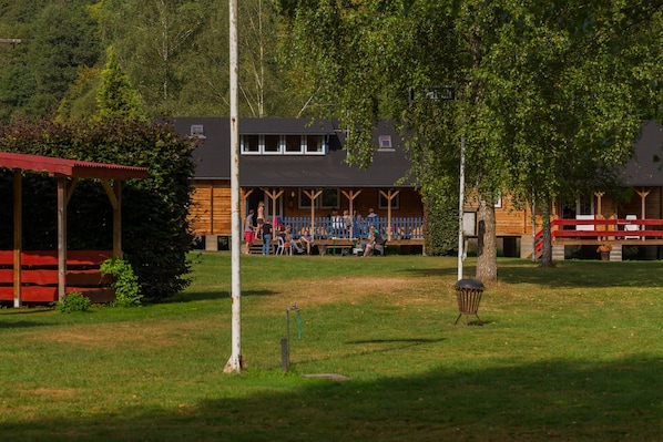 A rustic lodge with a wooden exterior, a covered deck, and a grassy lawn. - Dirbach Plage Parc (Esch-sur-Sure)