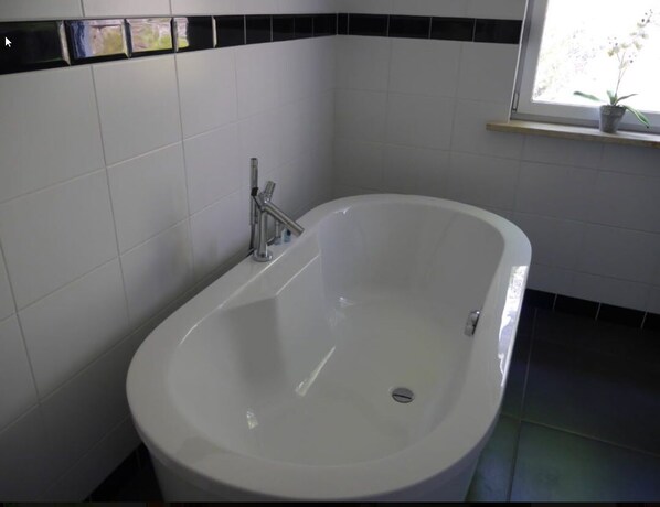 A bathroom with a white bathtub, black and white tiled walls, and a window with a plant on the sill. - Dirbach Plage Parc (Esch-sur-Sure)