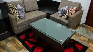 A living room with two sofas, a glass coffee table, and a patterned rug. - Sylva Link Suites (Lekki)