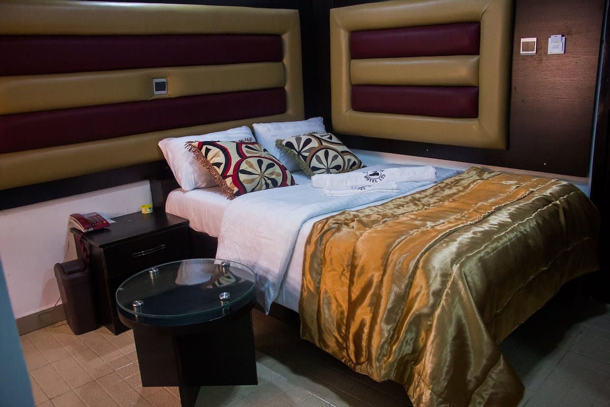 A hotel room with a bed, a bedside table, a lamp, and a nightstand.
