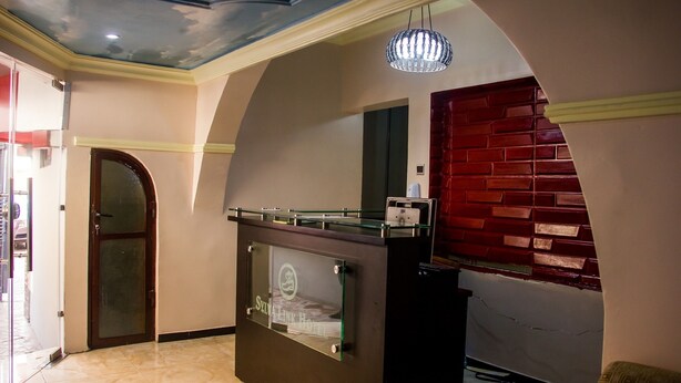 A reception area with a glass counter, a chandelier, a red brick wall, and a door. - Sylva Link Suites (Lekki)
