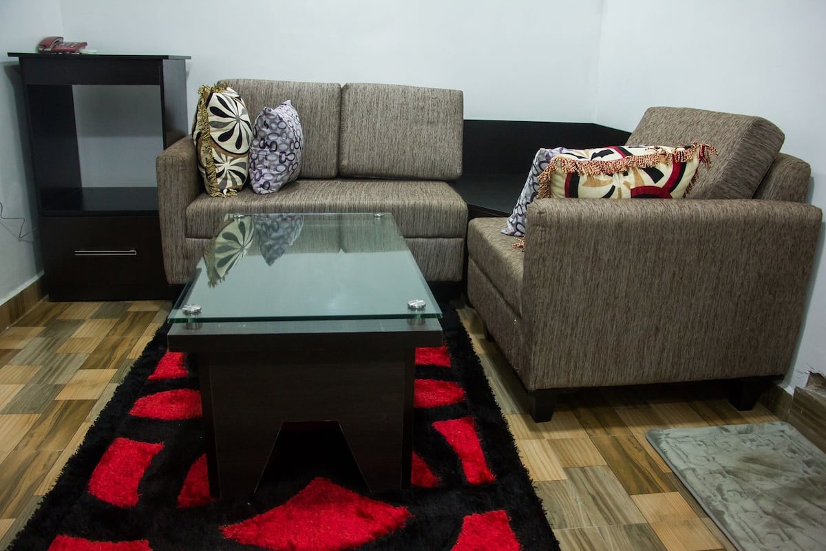 A living room with a glass coffee table, two sofas, a black TV stand, and a patterned rug.