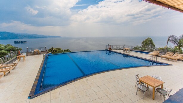 Una piscina con vistas al mar y a las montañas, rodeada de sillones y mesas.