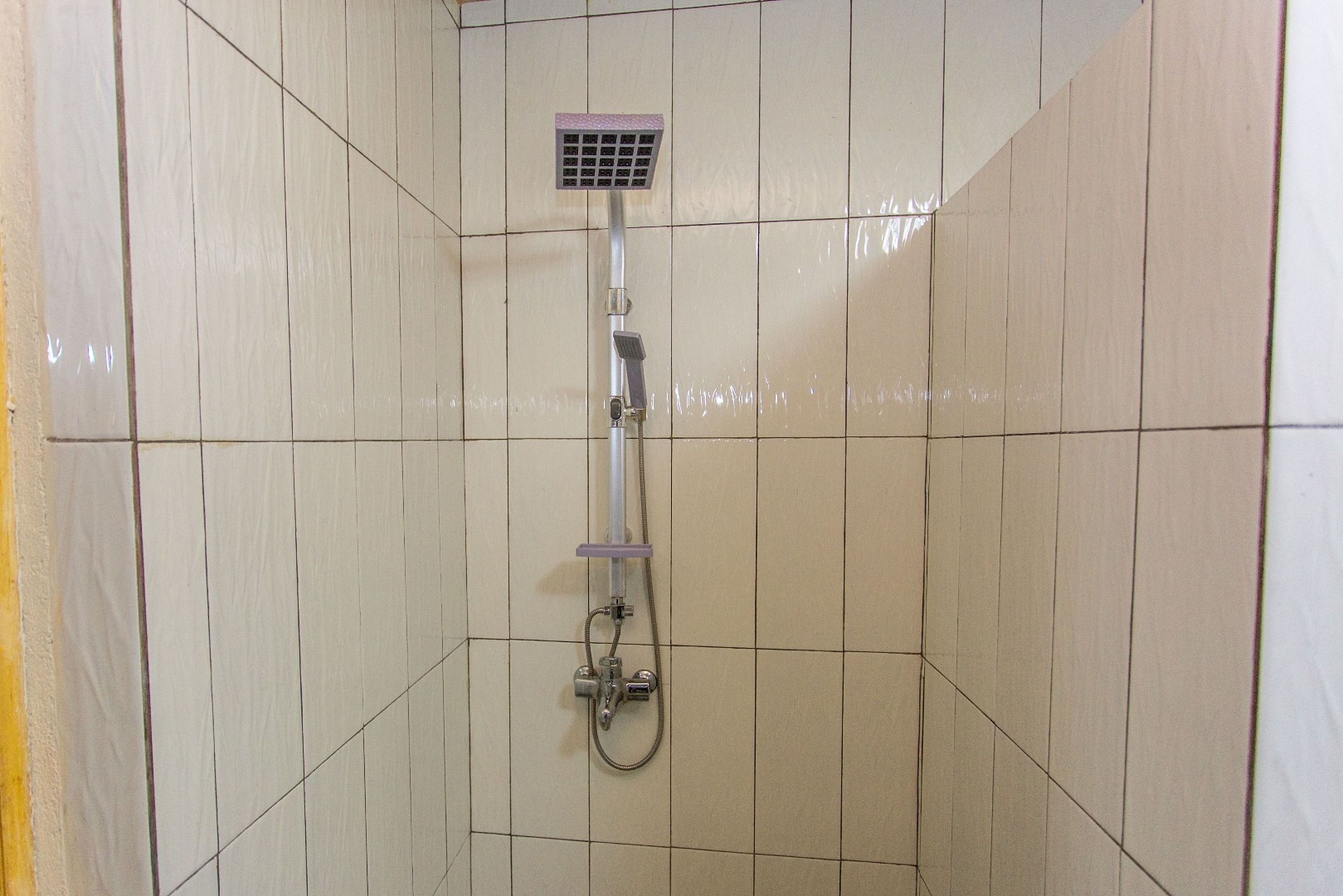 A shower with a handheld showerhead and a wall-mounted control panel.