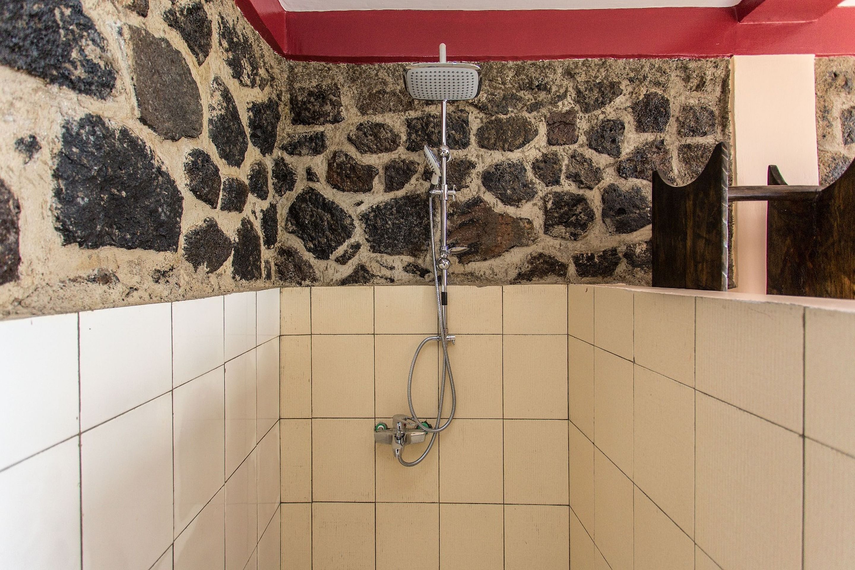 A shower area with a stone wall, tiled floor, and a red ceiling.