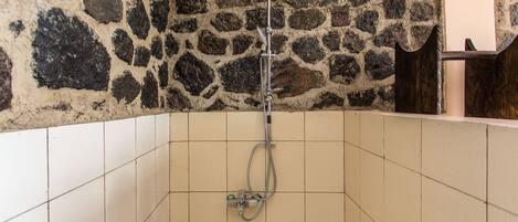A shower area with a stone wall, tiled floor, and a red ceiling.