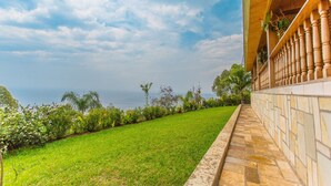 Un edificio con un camino de piedra que lleva a un balcón con barandillas de madera, con vistas a una zona cubierta de césped y diversas plantas y árboles.
