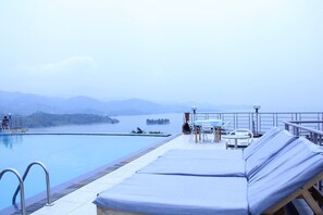 A poolside area with lounge chairs and a table, overlooking a body of water and distant hills. - Nirvana Heights Hotel (Nyayumba)