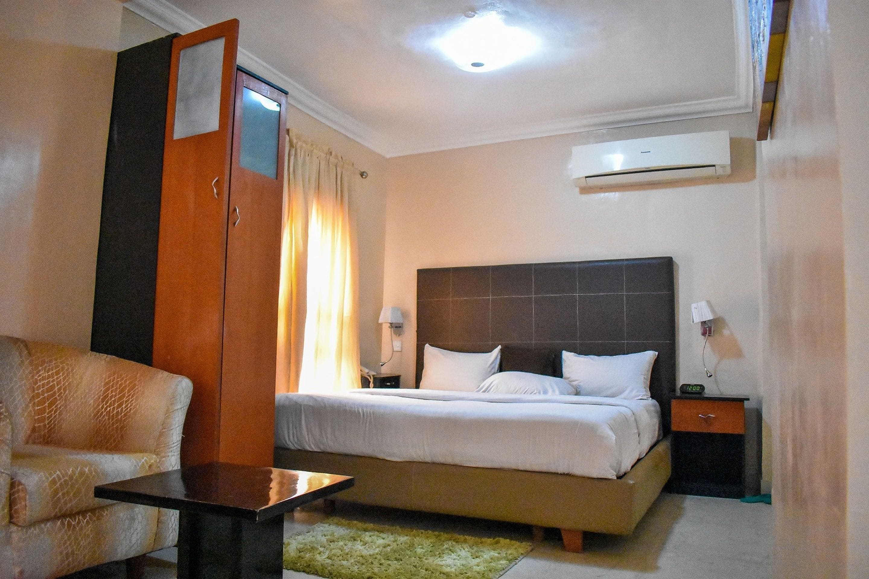 A hotel room with a bed, bedside table, lamp, and a chair.