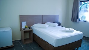 Habitación de hotel con cama, mesita de noche, una pequeña mesa, ventana con cortinas y vistas a zonas verdes.