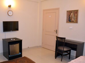 A room with a television, a desk, a chair, a door, and a clock on the wall.