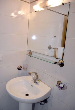 A bathroom with a white sink, a mirror, and a glass shelf.